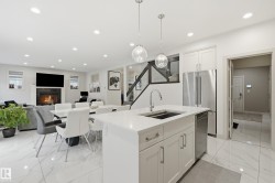 Open-concept living space with a central kitchen island featuring a stainless steel sink and pendant lighting - 