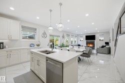 Open-concept living space featuring a central kitchen island with integrated sink, white cabinetry with silver hardware, recessed ceiling lighting, and large format white tile flooring throughout - 