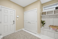 Entryway featuring a six-panel door with smart lock, white bi-fold closet doors, built-in mudroom bench with storage, overhead shelving, and white tile flooring - 