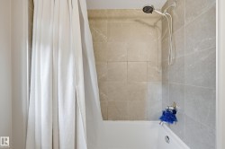 Bathtub and shower combination featuring neutral-toned tile surround, a rain shower head, and a hand-held shower fixture - 