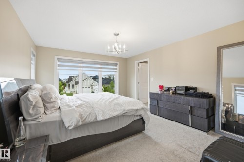 Spacious bedroom featuring neutral wall tones, plush carpeting, a large window with privacy blinds, and a contemporary chandelier - 76 Jacobs Close, St. Albert, AB 