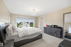 Spacious bedroom featuring neutral wall tones, plush carpeting, a large window with privacy blinds, and a contemporary chandelier - 