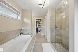 Contemporary bathroom featuring a large soaking tub with tiled surround, a spacious walk-in shower with glass enclosure and mosaic tile floor, and sophisticated overhead lighting fixtures - 
