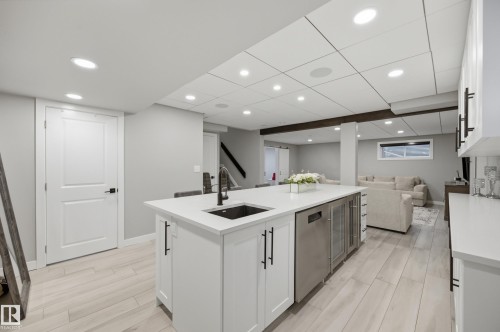 Spacious lower-level entertainment area featuring a large island with a built-in sink and beverage coolers, recessed lighting, and wood-finish flooring - 76 Jacobs Close, St. Albert, AB 