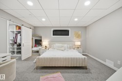Carpeted bedroom featuring a barn door entry to custom built-in shelving, a drop ceiling with recessed lighting, a horizontal window, and painted walls - 