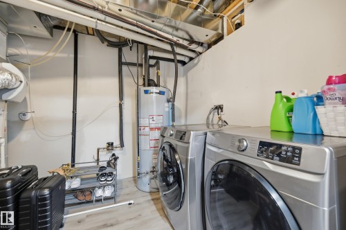 Dedicated laundry area featuring a front-loading washer and dryer set, water heater, exposed utility piping, and light wood-finish flooring - 76 Jacobs Close, St. Albert, AB 