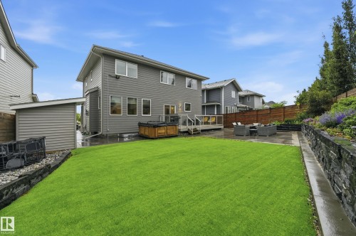 Expansive backyard featuring a manicured lawn, stone retaining wall, and a wood deck - 76 Jacobs Close, St. Albert, AB 