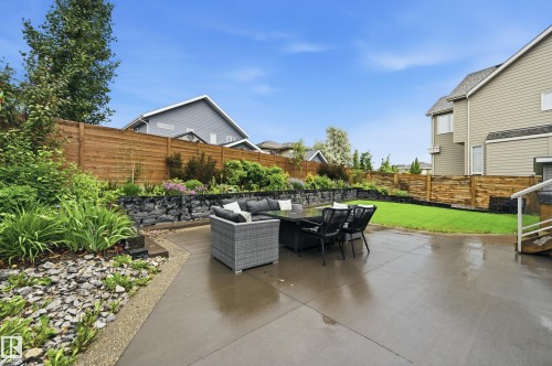 Expansive concrete patio area with a stone retaining wall and lush landscaping - 76 Jacobs Close, St. Albert, AB 