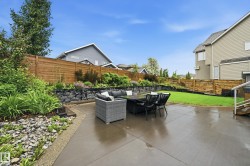 Expansive concrete patio area with a stone retaining wall and lush landscaping - 