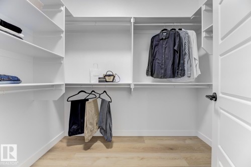 Walk-in closet featuring light wood-finish flooring, white built-in shelving, multiple hanging rods, and a white paneled door with a black handle - 519 Ashgrove Circle, Leduc, AB 