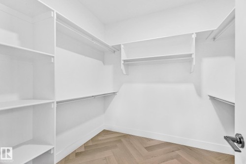 Walk-in closet featuring extensive white shelving, multiple hanging rods, durable baseboards, a herringbone wood-finish floor, and a contemporary door handle - 519 Ashgrove Circle, Leduc, AB 