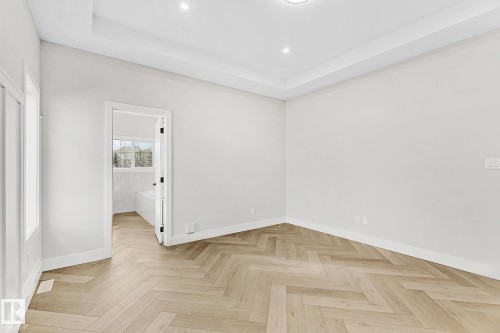 Spacious room featuring herringbone wood-finish flooring, a tray ceiling with recessed lighting, and a neutral color palette - 519 Ashgrove Circle, Leduc, AB 