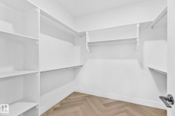 Walk-in closet featuring extensive white shelving, multiple hanging rods, durable baseboards, a herringbone wood-finish floor, and a contemporary door handle - 