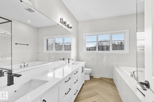 Dual vanity with white cabinetry and black hardware, complemented by a large integrated mirror and contemporary light fixture - 519 Ashgrove Circle, Leduc, AB 