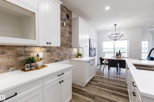 Contemporary kitchen featuring white cabinetry, light-toned countertops, and a brick-patterned backsplash - 519 Ashgrove Circle, Leduc, AB 