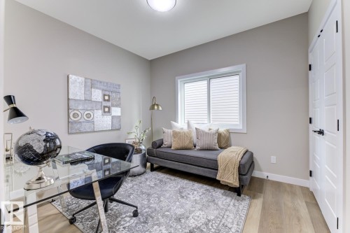 Well-lit interior space featuring neutral wall tones, wood-finish flooring, a contemporary window with blinds, a white paneled door with black hardware, and a ceiling-mounted light fixture - 519 Ashgrove Circle, Leduc, AB 