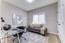 Well-lit interior space featuring neutral wall tones, wood-finish flooring, a contemporary window with blinds, a white paneled door with black hardware, and a ceiling-mounted light fixture - 519 Ashgrove Circle, Leduc, AB 