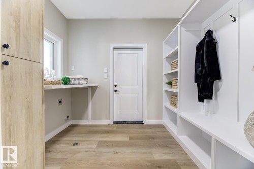 Functional utility room featuring wood-finish flooring, built-in white shelving, integrated coat hooks, a window for natural light, and a dedicated counter area - 519 Ashgrove Circle, Leduc, AB 