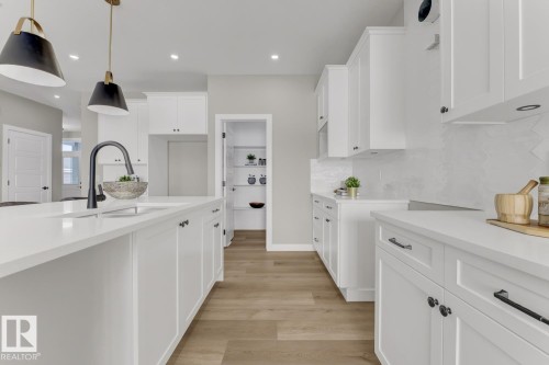 Contemporary kitchen featuring an expansive center island with an undermount sink and matte black faucet, recessed lighting, wood-finish flooring, white shaker cabinetry, and a walk-in pantry - 519 Ashgrove Circle, Leduc, AB 