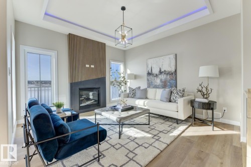 Contemporary living space featuring a tray ceiling with recessed lighting, a fireplace with a dark tile surround and wood paneling, wood-finish flooring, and multiple windows - 519 Ashgrove Circle, Leduc, AB 