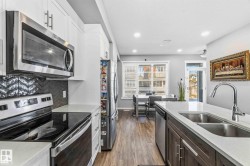 Modern kitchen featuring stainless steel appliances, white upper cabinetry, dark wood-finish lower cabinetry, white countertops, and wood-finish flooring - 
