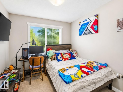 Bedroom featuring a large window with horizontal blinds, light beige carpeting, and a wood-finish bed frame with a dark headboard - 1908 25 Street, Edmonton, AB 