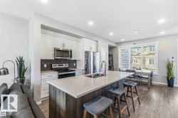 Modern kitchen with stainless steel appliances, white cabinetry, a dark herringbone tile backsplash, and a large island with an integrated double sink - 