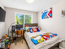 Bedroom featuring a large window with horizontal blinds, light beige carpeting, and a wood-finish bed frame with a dark headboard - 