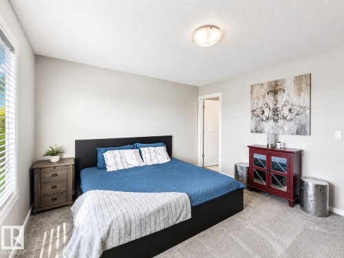 Carpeted bedroom featuring neutral wall tones, a large window with blinds, and a semi-flush ceiling light fixture - 1908 25 Street Nw, Edmonton, AB 