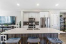 Kitchen featuring a large central island with an undermount sink, white cabinetry, stainless steel appliances, and a herringbone-patterned tile backsplash - 1908 25 Street, Edmonton, AB 