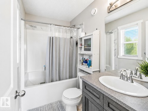 Full bathroom featuring a white tub with subway tile surround, a dark wood-finish vanity with a light-toned countertop, and a white oval sink with brushed nickel fixtures - 1908 25 Street Nw, Edmonton, AB 