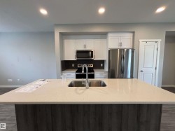 Spacious kitchen island with a built-in sink and light-toned countertop, complemented by white cabinetry and stainless steel appliances - 