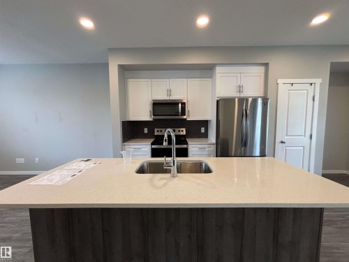 Spacious kitchen island with a built-in sink, stainless steel appliances, white cabinetry, and wood-finish flooring - 1908 25 Street Nw, Edmonton, AB 
