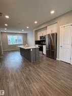 Kitchen featuring a central island with a sink, stainless steel appliances, white cabinetry, and wood-finish flooring - 