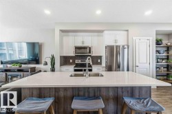 Kitchen featuring a large central island with an undermount sink, white cabinetry, stainless steel appliances, and a herringbone-patterned tile backsplash - 