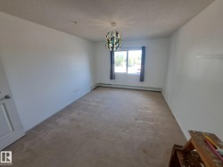 Spacious room featuring neutral carpeting, white walls, and a large window with dark drapes - 