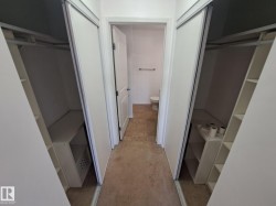 Hallway featuring sliding closet doors with built-in shelving, hanging rods, and an open doorway to a bathroom with tile flooring - 