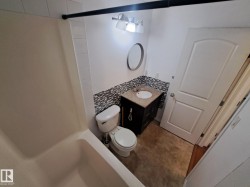 Bathroom featuring a dark wood-finish vanity with an undermount sink and speckled countertop, mosaic tile backsplash, and a white tub/shower combination with white subway tile surround - 