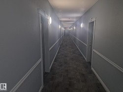 Long hallway featuring textured gray walls, decorative wainscoting, recessed ceiling lighting, and wall-mounted sconces - 