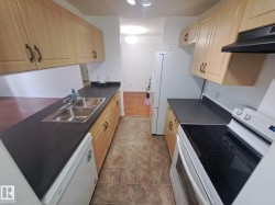 Galley kitchen featuring light wood-finish cabinetry, dark countertops, and a double basin stainless steel sink - 