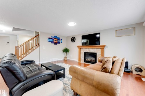 Living area featuring wood-finish flooring, a prominent fireplace with a tiled surround and wood mantel, and a staircase with wooden railing - 3012 25 Ave Avenue, Edmonton, AB 