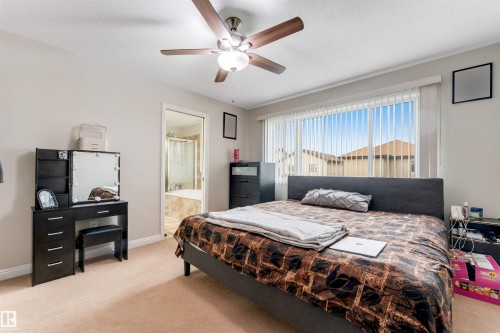 Carpeted bedroom with a ceiling fan, large window with vertical blinds, and a doorway revealing a bathroom with a built-in tub - 3012 25 Ave Avenue, Edmonton, AB 