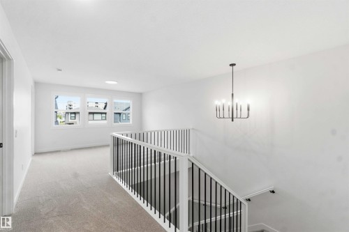 Upper-level landing featuring a contemporary chandelier, white walls, and light-toned carpeting - 1085 Cristall Crescent, Edmonton, AB 