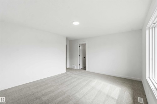 Spacious room featuring light gray carpeting, neutral wall finishes, a large window, a recessed ceiling light, and a white interior door with dark hardware - 1085 Cristall Crescent, Edmonton, AB 