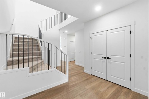 Two-story foyer featuring contemporary black metal balusters, light wood-finish flooring, recessed lighting, and white paneled doors with matte black hardware - 1085 Cristall Crescent, Edmonton, AB 