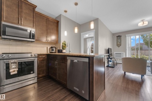 Open-concept kitchen featuring wood-finish cabinetry, stainless steel appliances, pendant lighting, and a durable countertop - 115 812 Welsh Drive Sw, Edmonton, AB 