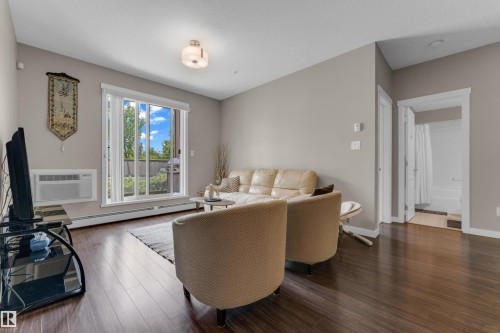 Living area featuring dark wood-finish flooring, neutral wall tones, and a large sliding glass door - 115 812 Welsh Drive Sw, Edmonton, AB 