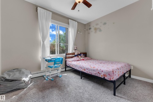 Bedroom featuring neutral wall tones, large window with white trim, and a ceiling fan with integrated lighting - 115 812 Welsh Drive Sw, Edmonton, AB 