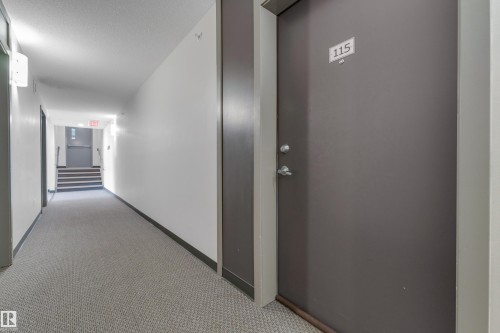 Property entrance featuring a solid door with modern hardware, leading to a hallway with patterned carpeting - 115 812 Welsh Drive Sw, Edmonton, AB 