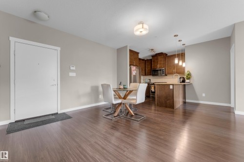 Open-concept living space featuring wood-finish flooring, a kitchen with rich wood cabinetry, stainless steel appliances, a breakfast bar, and pendant lighting - 115 812 Welsh Drive Sw, Edmonton, AB 